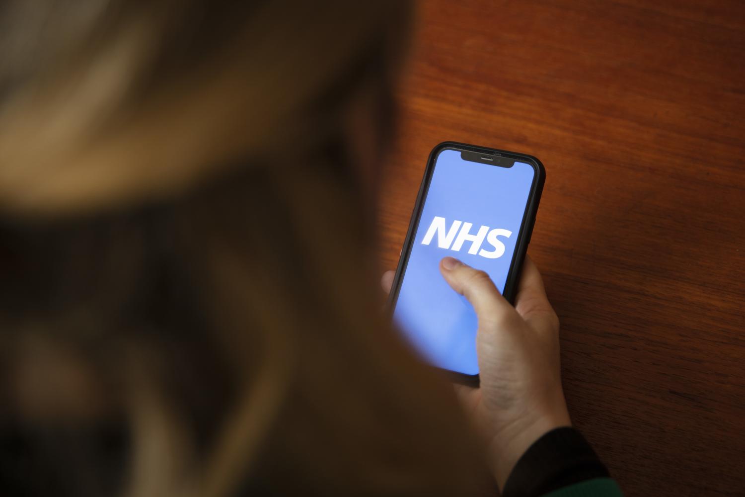 women looking at a mobile displaying the NHS logo
